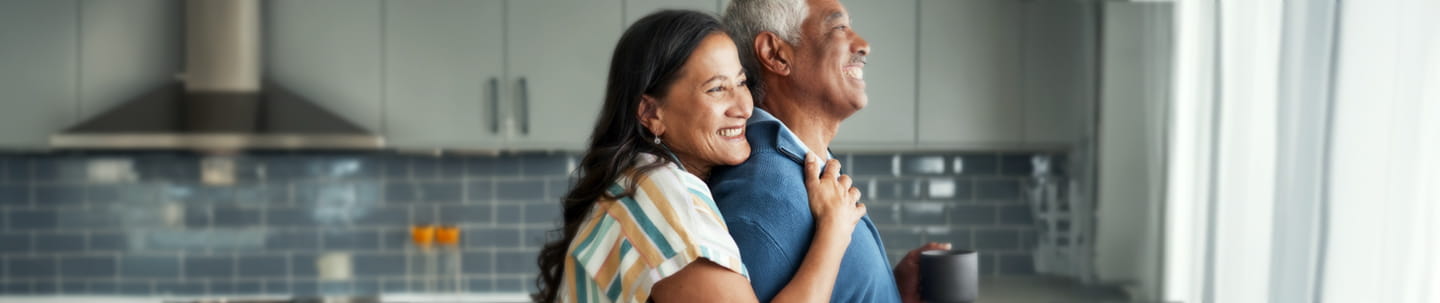 Woman embracing man while both look out the window in a kitchen 